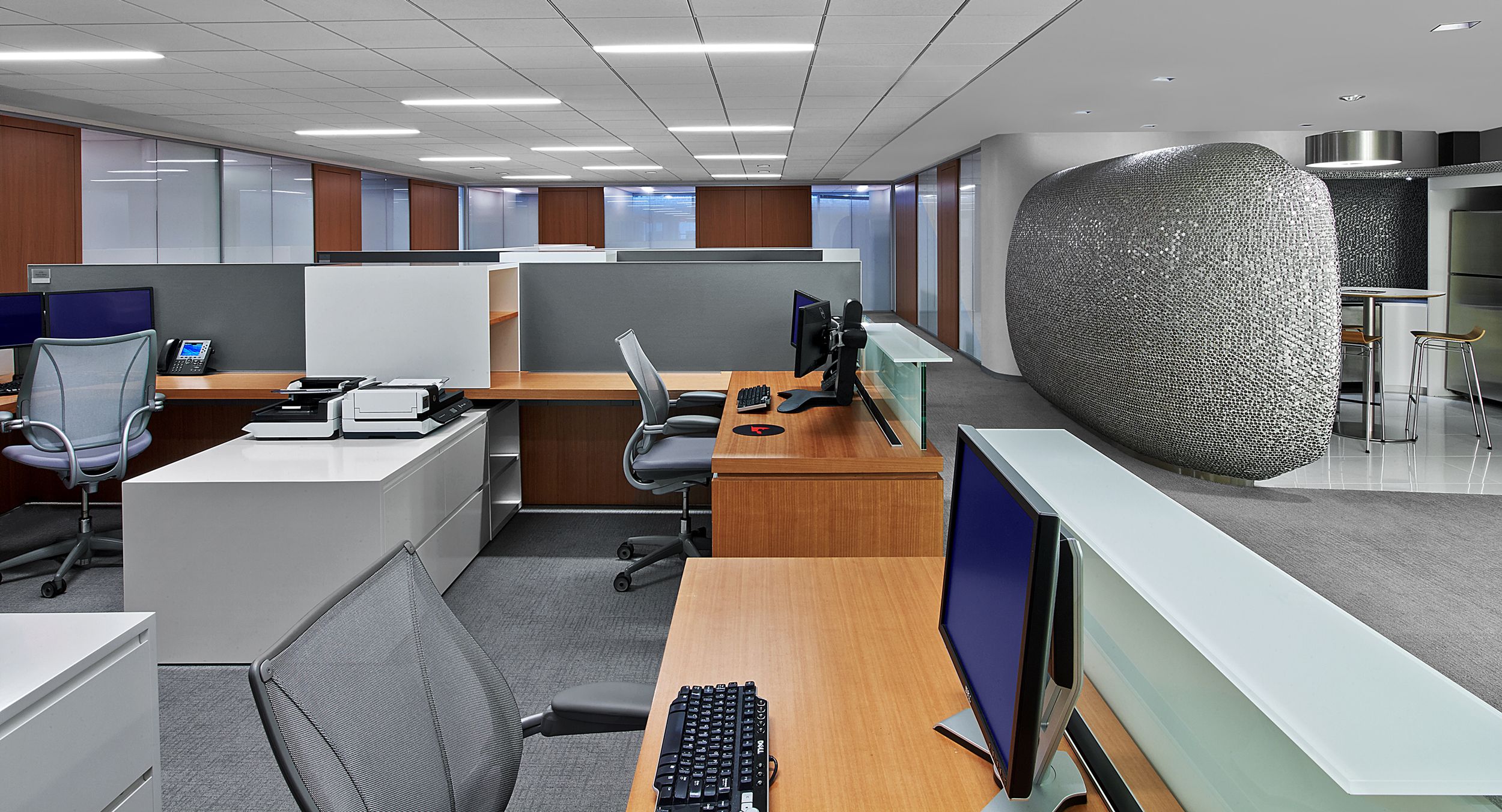 Custom-designed workstations incorporate anigre veneers with white casework, aluminum-framed Forbo screens, and floating glass transaction counters.