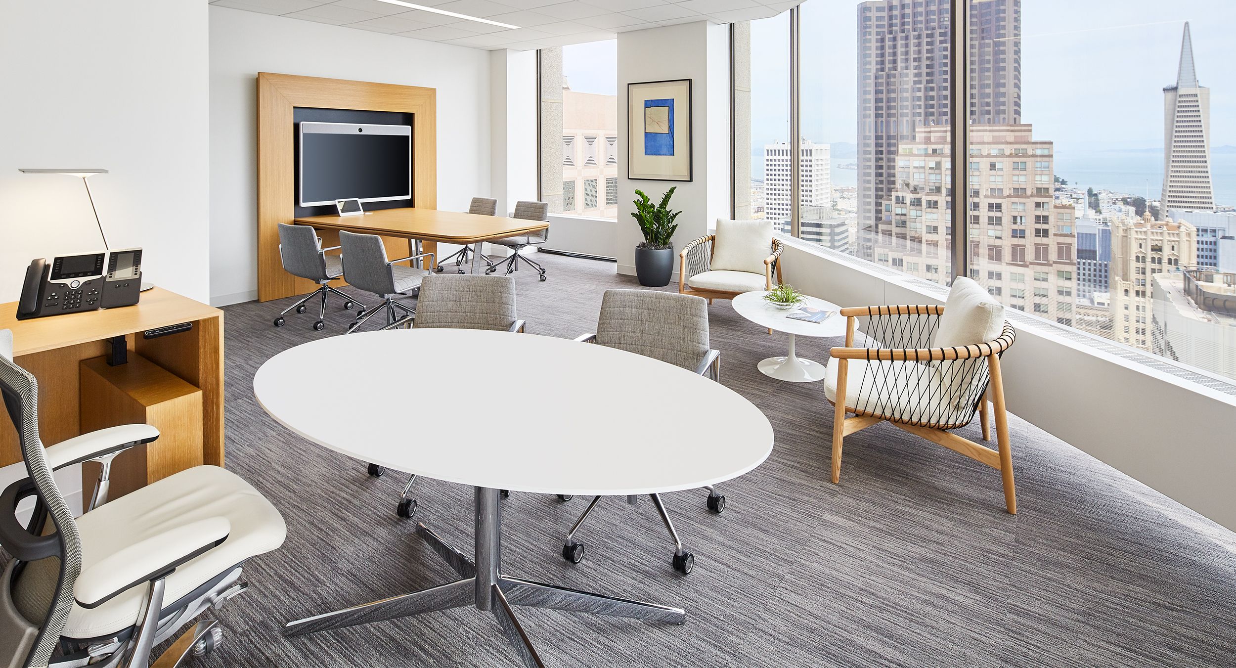 This SESSIONS elliptical table features a Modern White Corian® surface and a MESA media wall is finished in Rift White Oak and Polished Chrome.